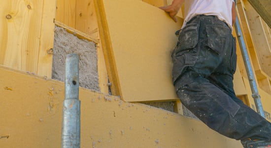 Pose de panneaux de bois d'isolation sur un mur en CLT rempli de ouate de cellulose